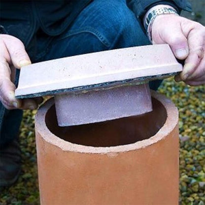 A person is placing a beige concrete plug into the top of a brown ceramic chimney pot.
